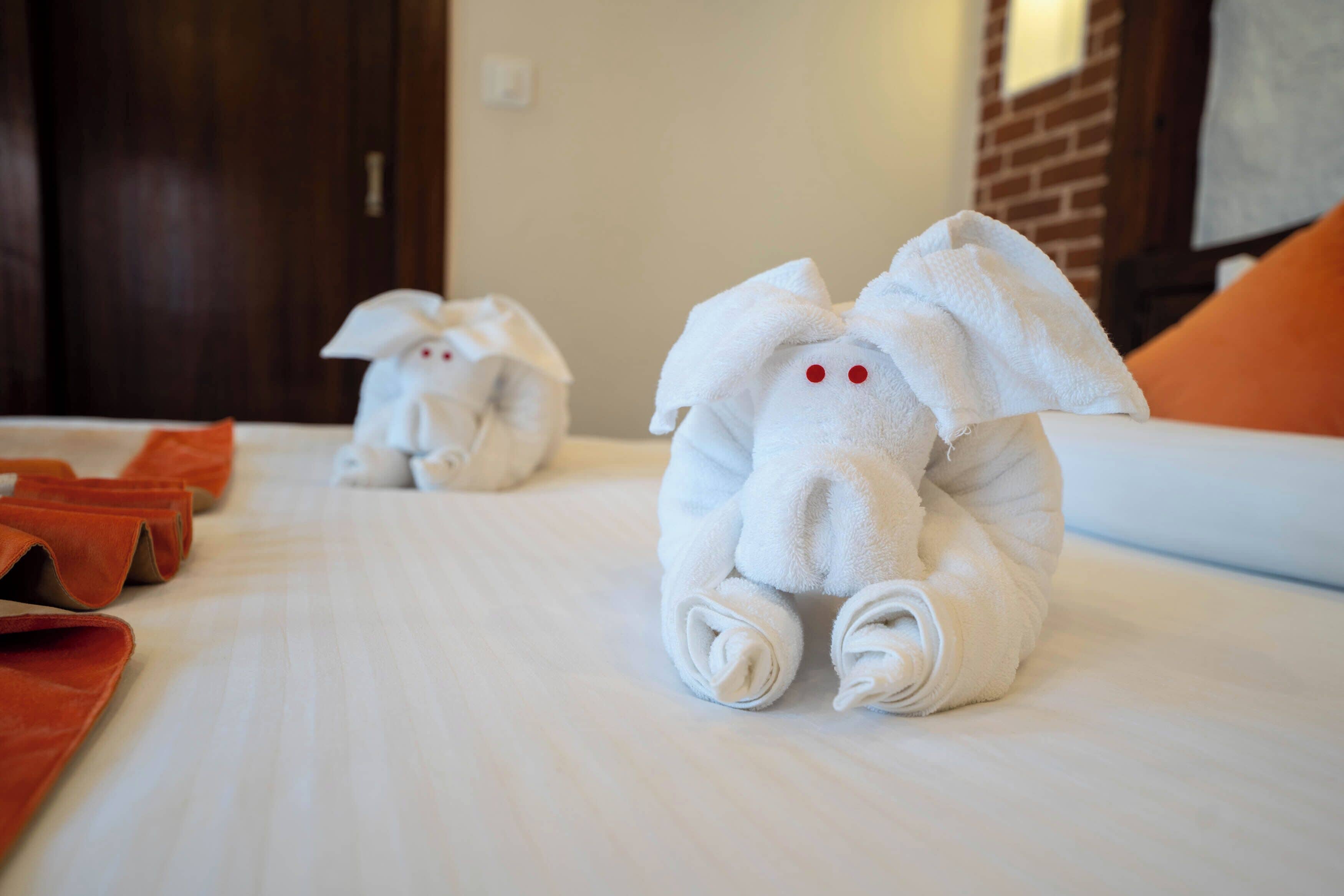 A hotel room with neatly folded towels shaped like animals on the bed.
