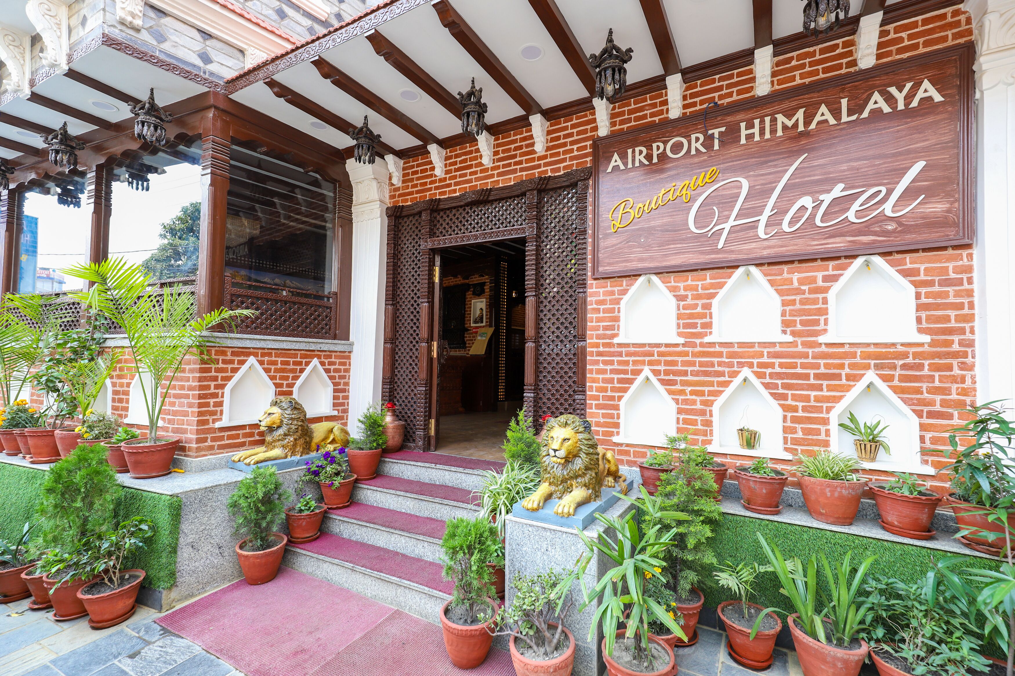 The exterior of the Airport Himalaya Boutique Hotel with a brick facade, decorative lion statues, and potted plants.