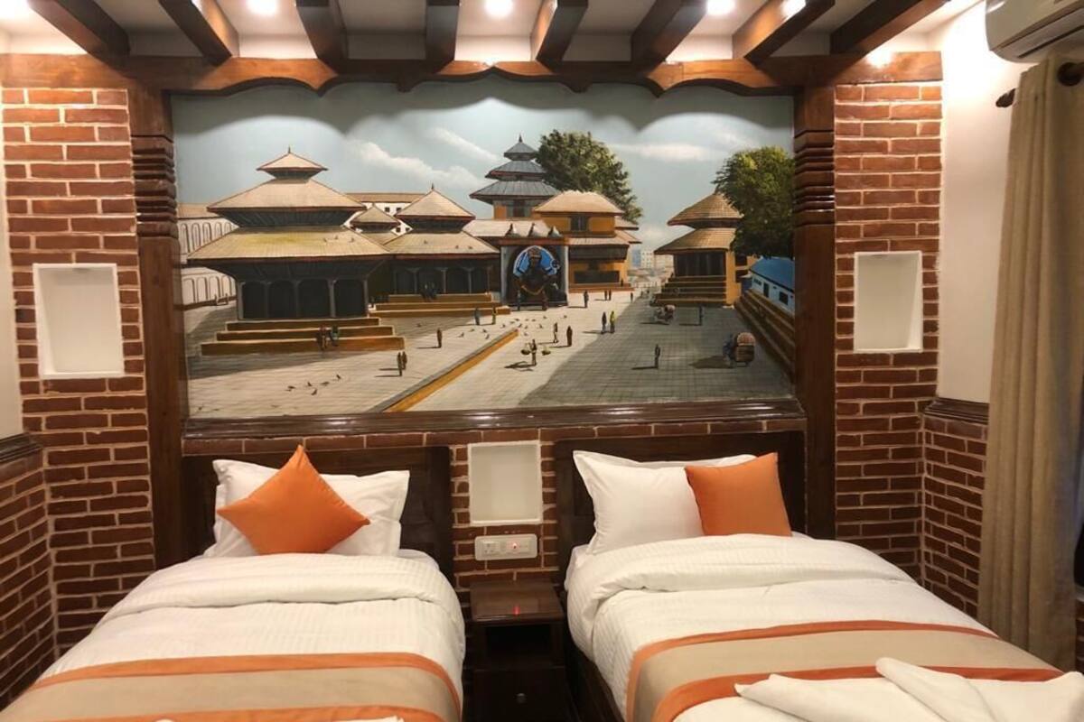 A hotel room with two beds, a mural of a traditional building, and brick walls.