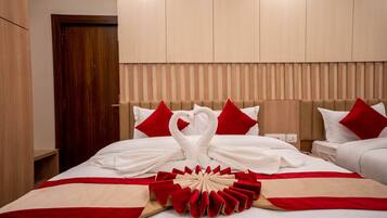 A hotel room with a bed featuring a red and white swan towel arrangement, a red and beige decorative pillow, and a wooden headboard.