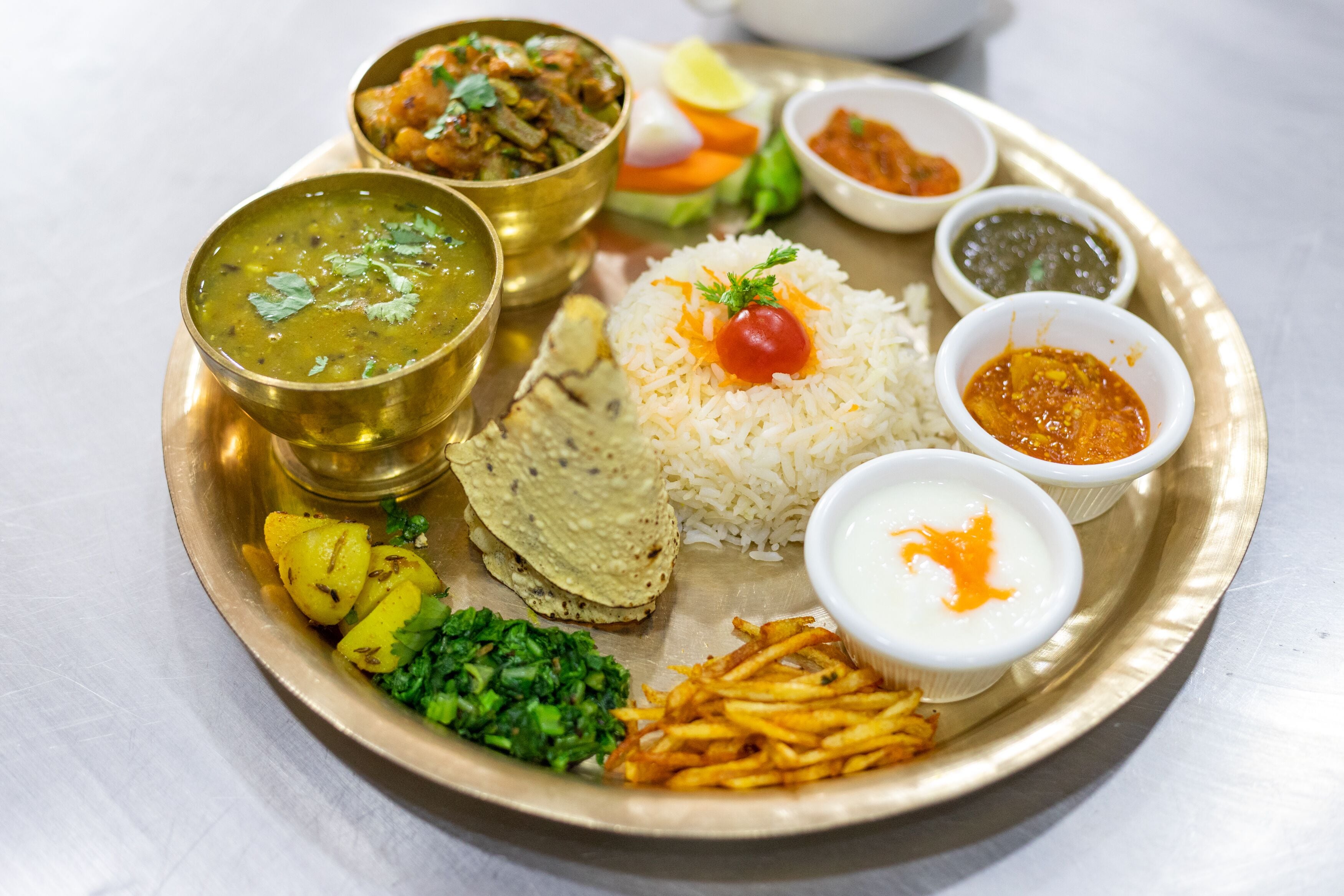 A traditional Indian meal served on a brass plate, including rice, dal, paneer, potato salad, and various chutneys.