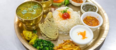 A traditional Indian meal served on a brass plate, including rice, dal, paneer, potato salad, and various chutneys.