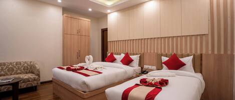 A hotel room with two beds, a sofa, wooden flooring, and a ceiling with recessed lighting.