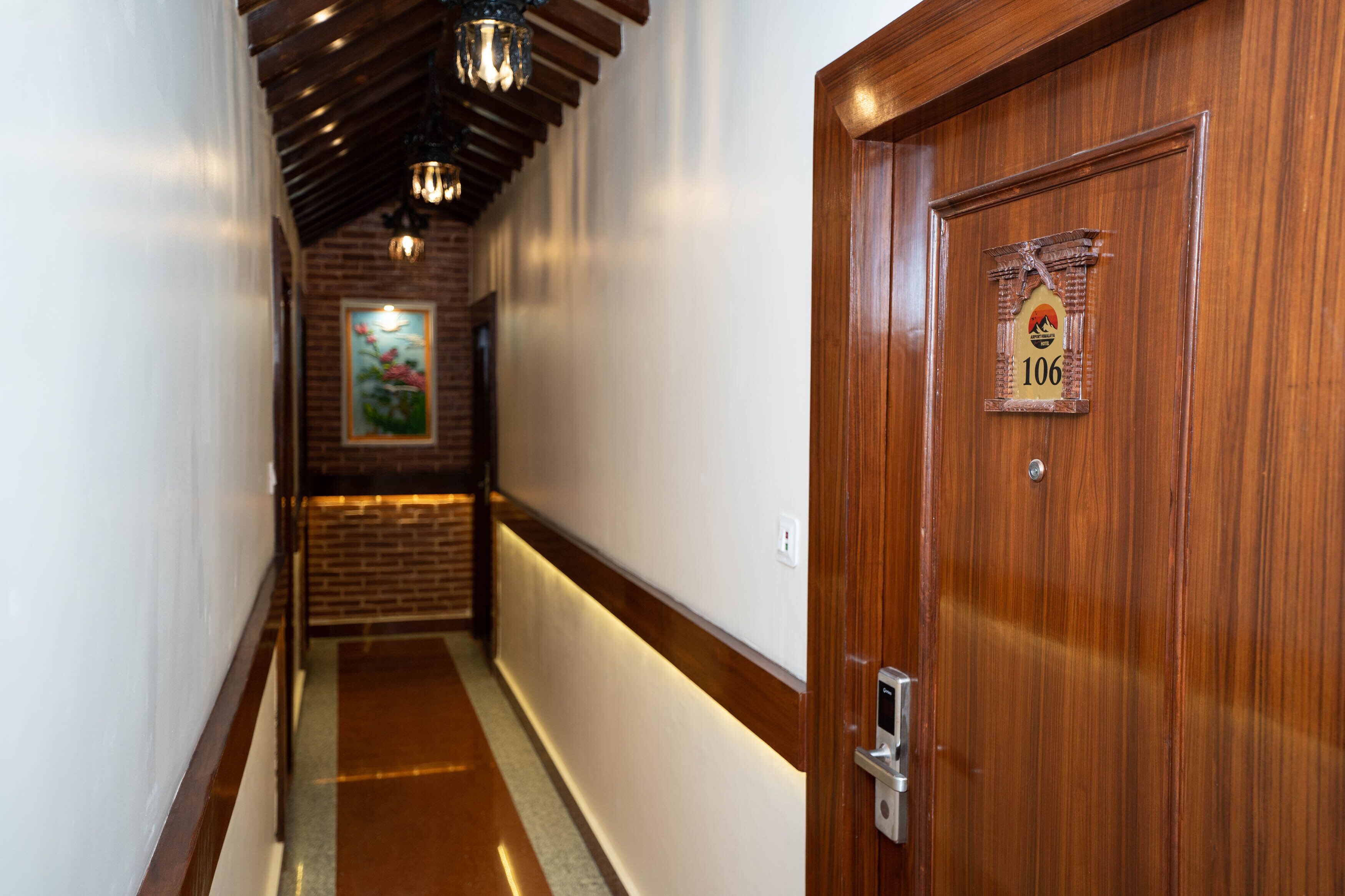 Un pasillo con una puerta de madera con el número 106 y una pared de ladrillo con un cuadro enmarcado.