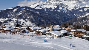 Eine verschneite Bergstadt mit traditionellen Holzhäusern, einer Kirche und einer Skipiste.