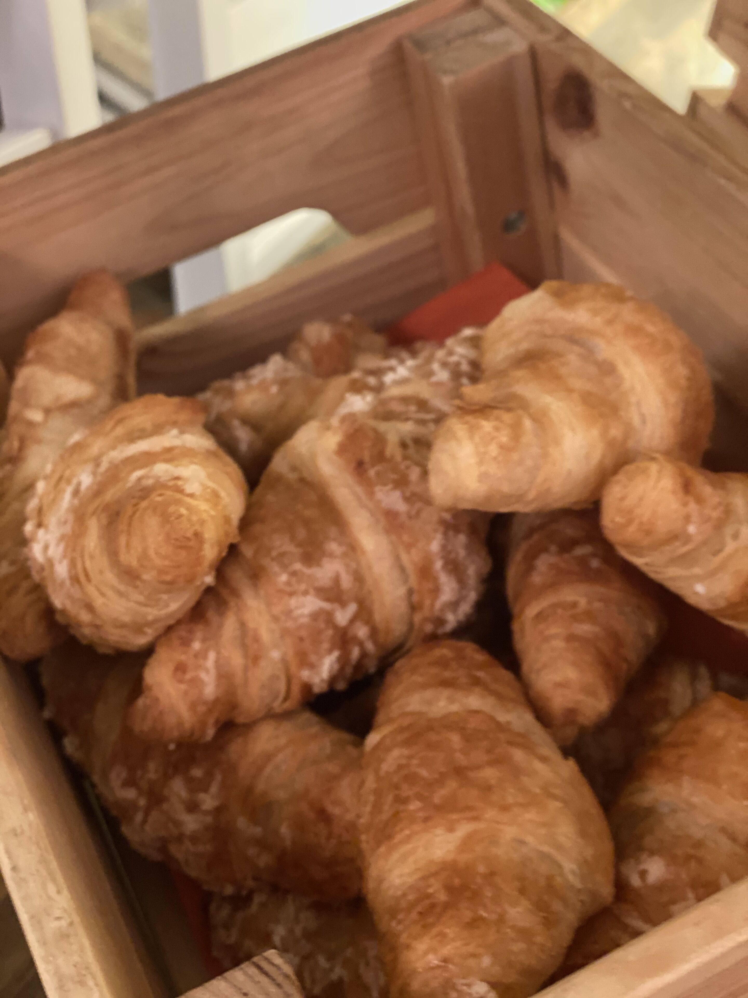 Una caja de madera llena de cruasanes dorados y tostados.