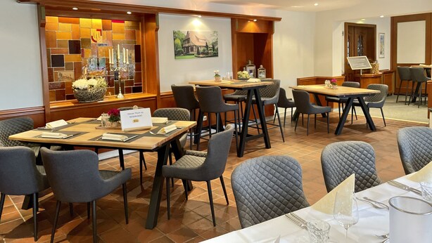 Uma área de refeições de hotel com várias mesas e cadeiras, uma parede decorativa com mosaico e uma placa indicando uma mesa reservada.