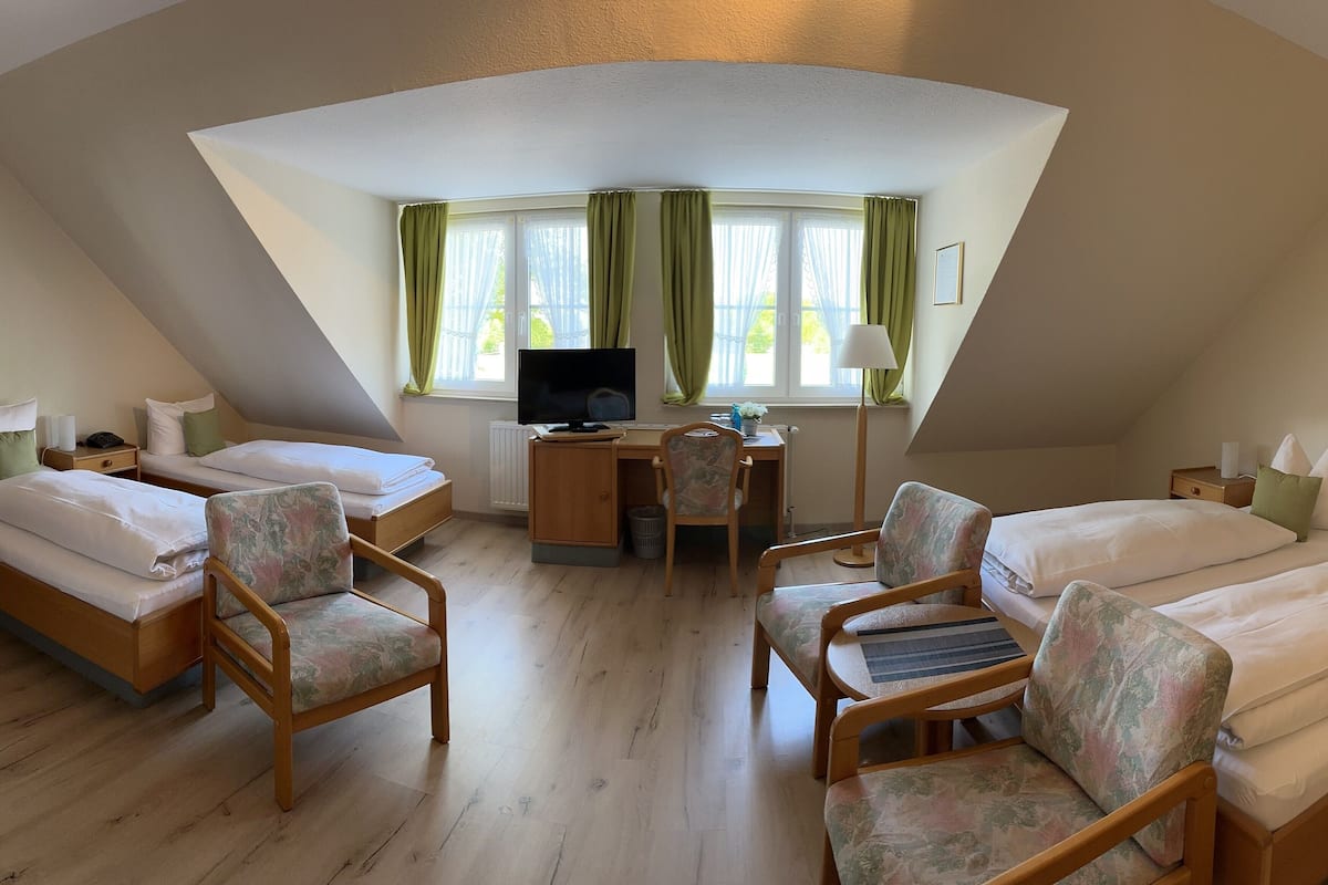 A cozy, triangular room with two beds, a desk, and a chair.