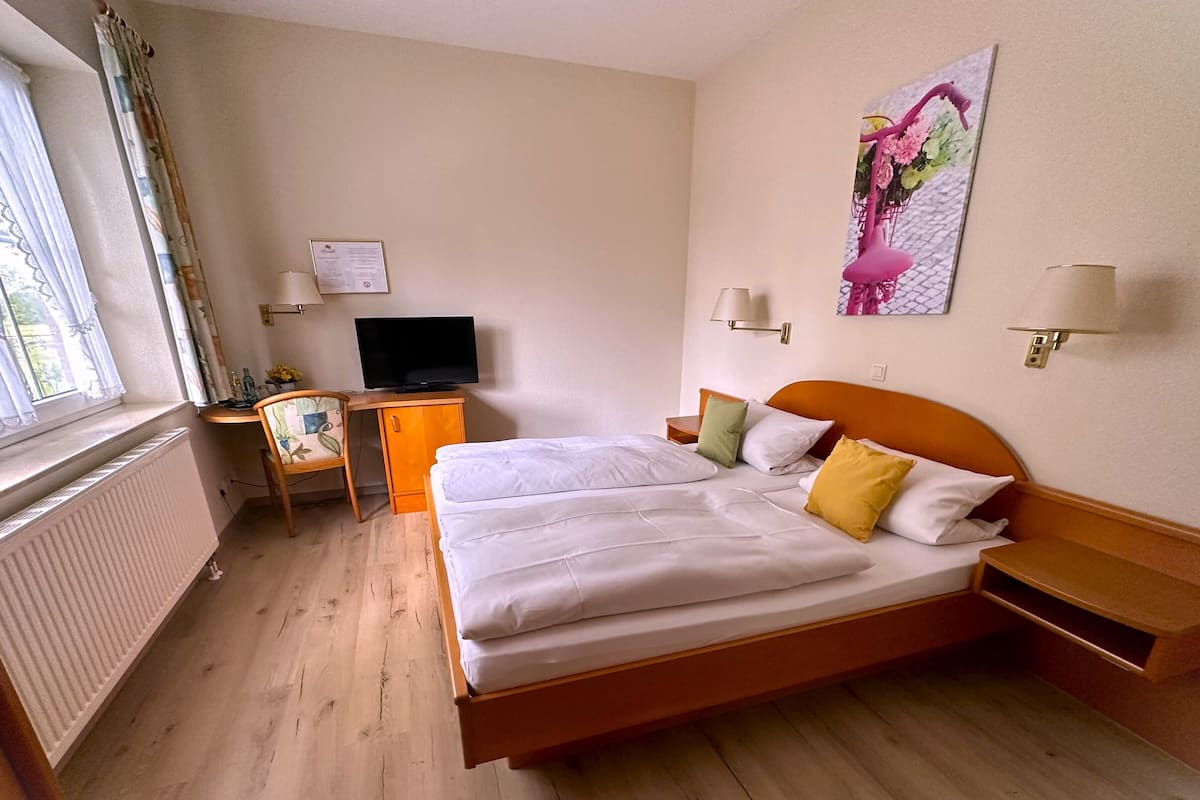A hotel room with a bed, a desk with a TV, a chair, and a window with curtains.