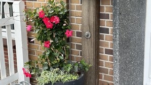 Um edifício com fachada de tijolos, uma grande planta em vaso com flores cor-de-rosa e uma placa indicando o endereço "2 Treldor Dorfstrasse Vessens Hoff".