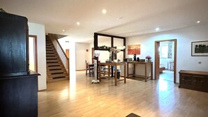 Uma sala de estar ampla com piso de madeira, uma mesa de jantar e uma cozinha ao fundo.