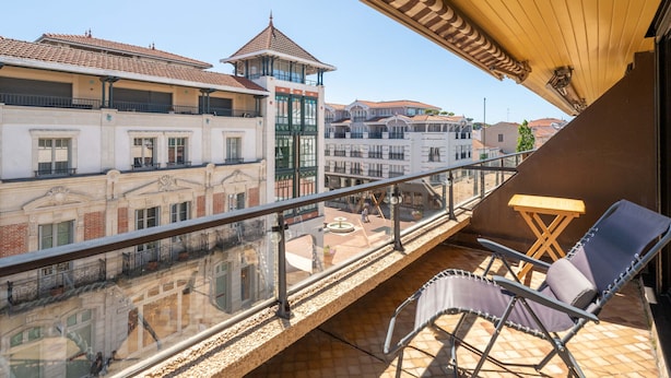 A balcony with a view of a building with a tiled roof, a glass railing, and a chair. - "Charming Studio in Central Arcachon with Balcony, Steps from Beach - Sleeps 2" (Arcachon)
