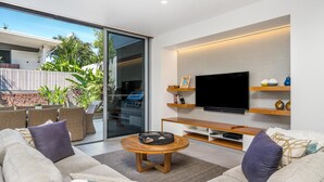 Un salon moderne doté d’un grand téléviseur à écran plat, de sièges confortables et d’une porte vitrée donnant sur un espace extérieur.