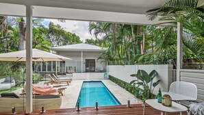 Un espace piscine aménagé avec des chaises longues, une table et une vue sur une maison et la végétation environnante.