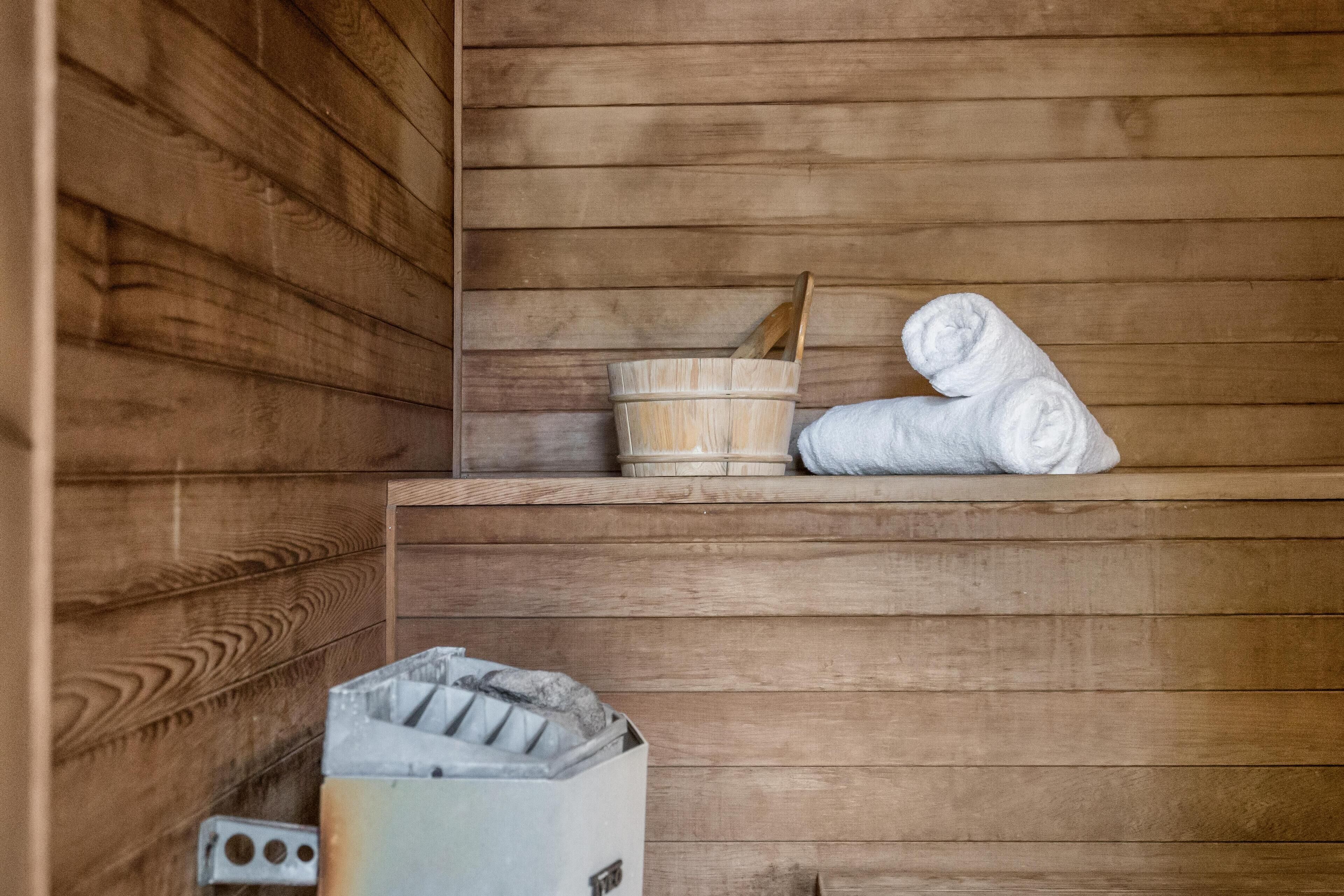 A sauna room with wooden walls, a wooden bucket, and a white towel.