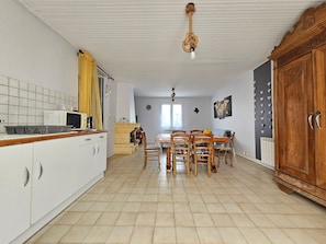 Una cocina con armarios blancos, una mesa de comedor con sillas, un aparador de madera y una lámpara colgante.