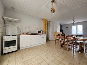 Una cocina con armarios blancos, estufa, microondas y un comedor con sillas de madera y una mesa.