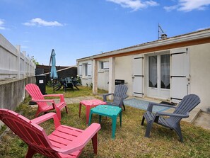 Un patio con mobiliario exterior, una mesita y un edificio de fachada blanca y una ventana.