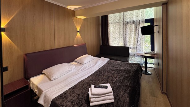 Habitación de hotel con una cama grande, una mesita de noche, una silla, un escritorio con lámpara y una ventana con cortinas.