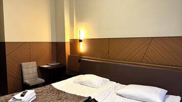 Una habitación de hotel con cama, una silla, una mesita de noche y una lámpara fijada a la pared.
