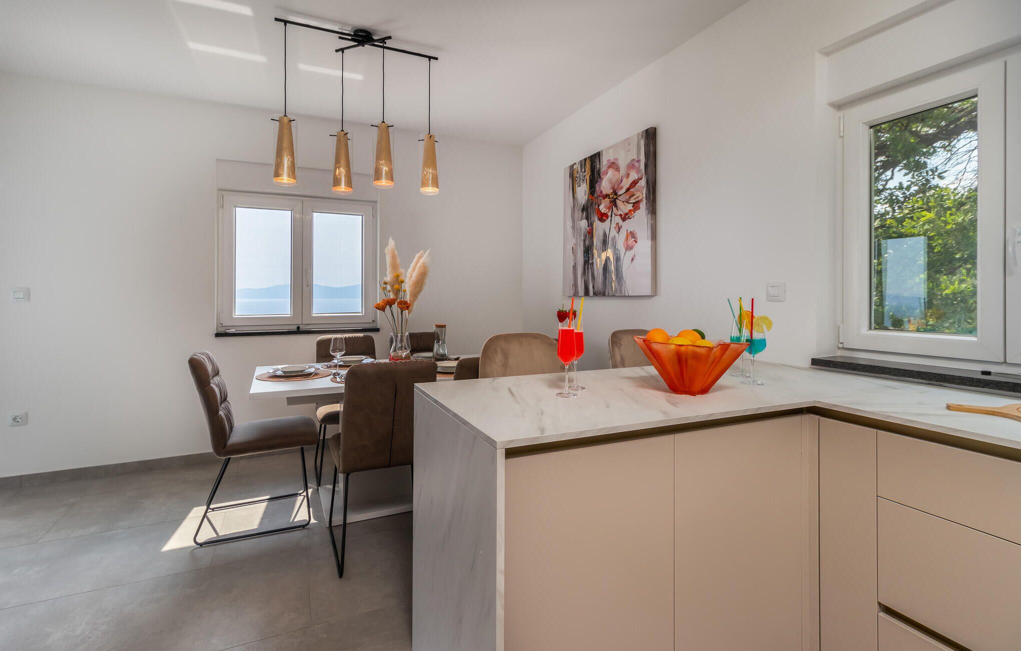 Una cucina moderna con isola centrale, lampade a sospensione e zona pranzo con sedie e tavolo.