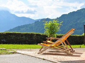 Una silla de madera en un área pavimentada con vistas a colinas verdes y un cielo despejado.