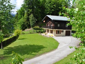 A two-story chalet with a balcony, surrounded by a well-maintained lawn and trees.