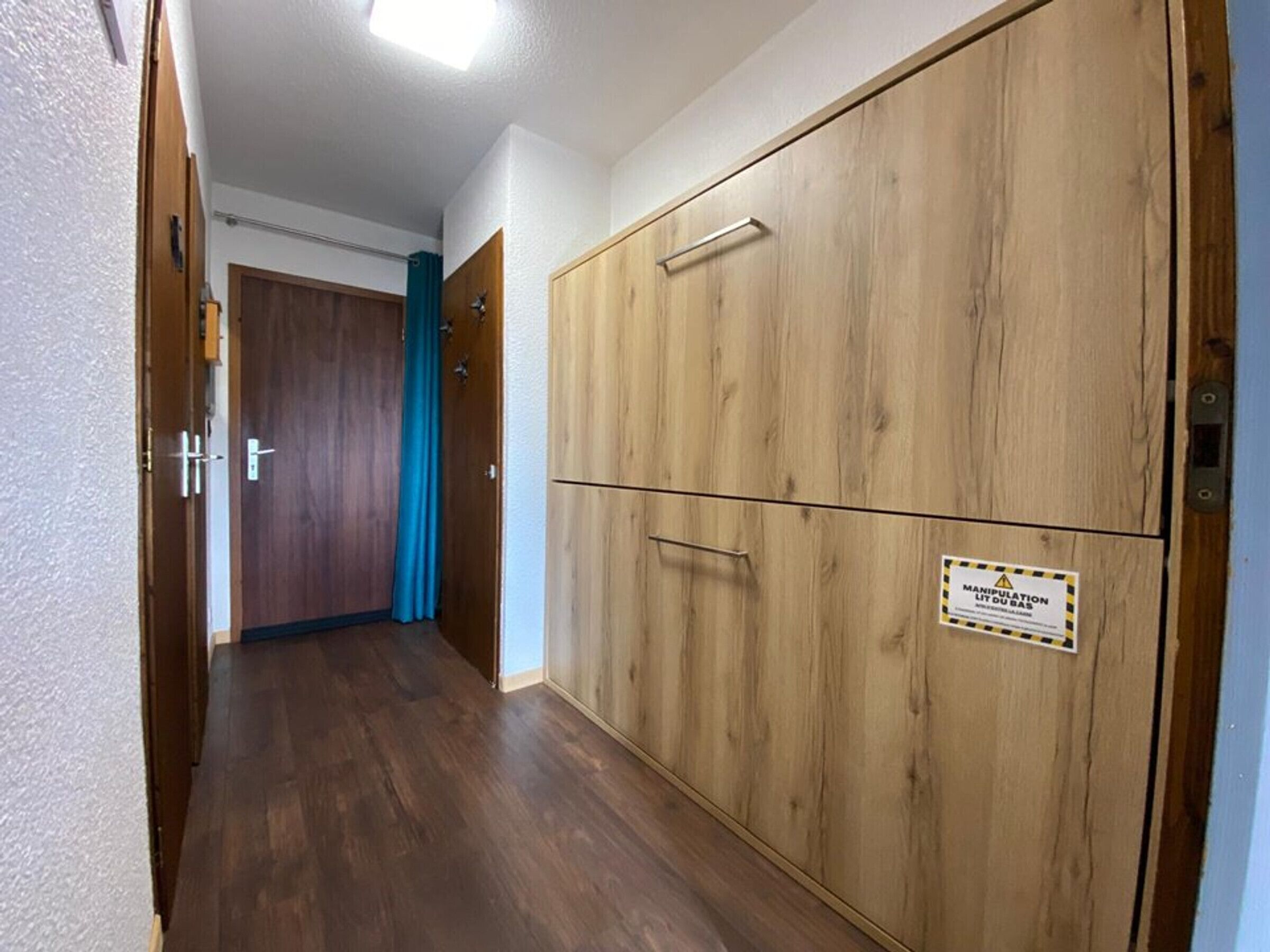Um corredor com portas de madeira, uma cortina azul e um aviso numa porta.