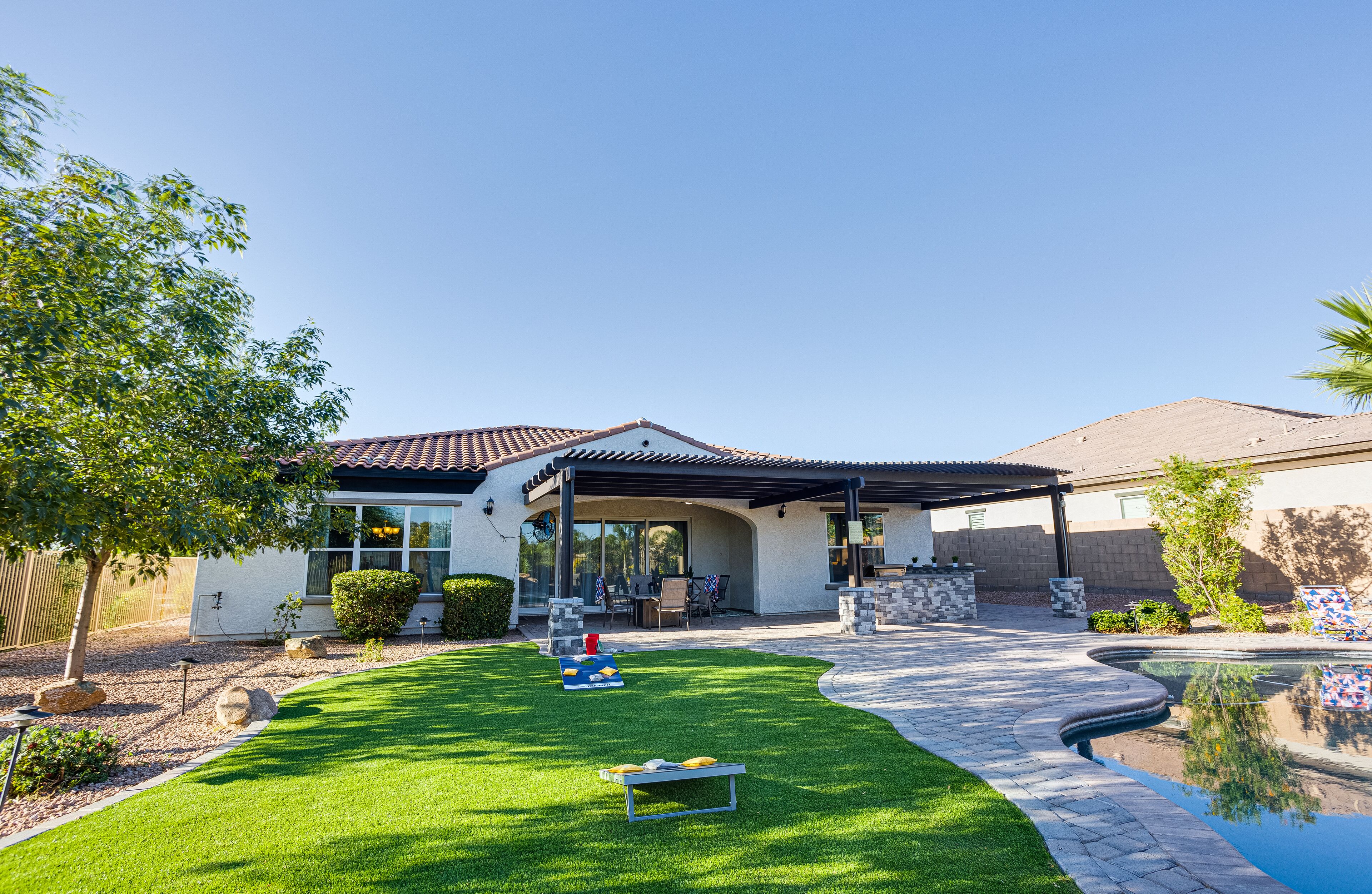 A modern house with a covered patio, a swimming pool, and a well-maintained lawn.