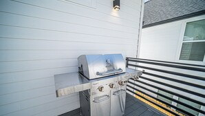 Un barbecue en acier inoxydable sur un balcon doté d’une rambarde, avec un immeuble blanc en arrière-plan.