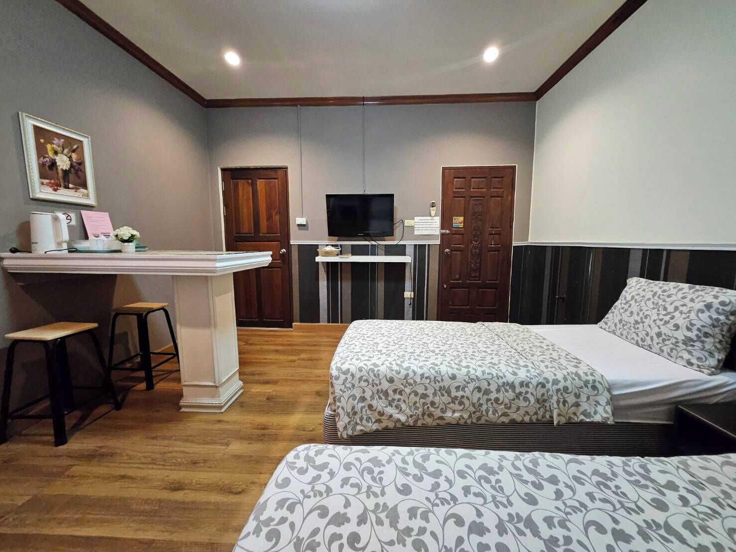 A hotel room with two beds, a desk with a chair, a television, and a small kitchenette.