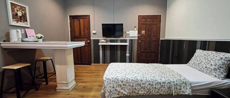 A hotel room with two beds, a desk with a chair, a television, and a small kitchenette.