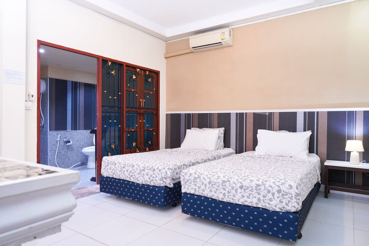 Habitación de hotel con dos camas, un baño y una pequeña mesa con lámpara.
