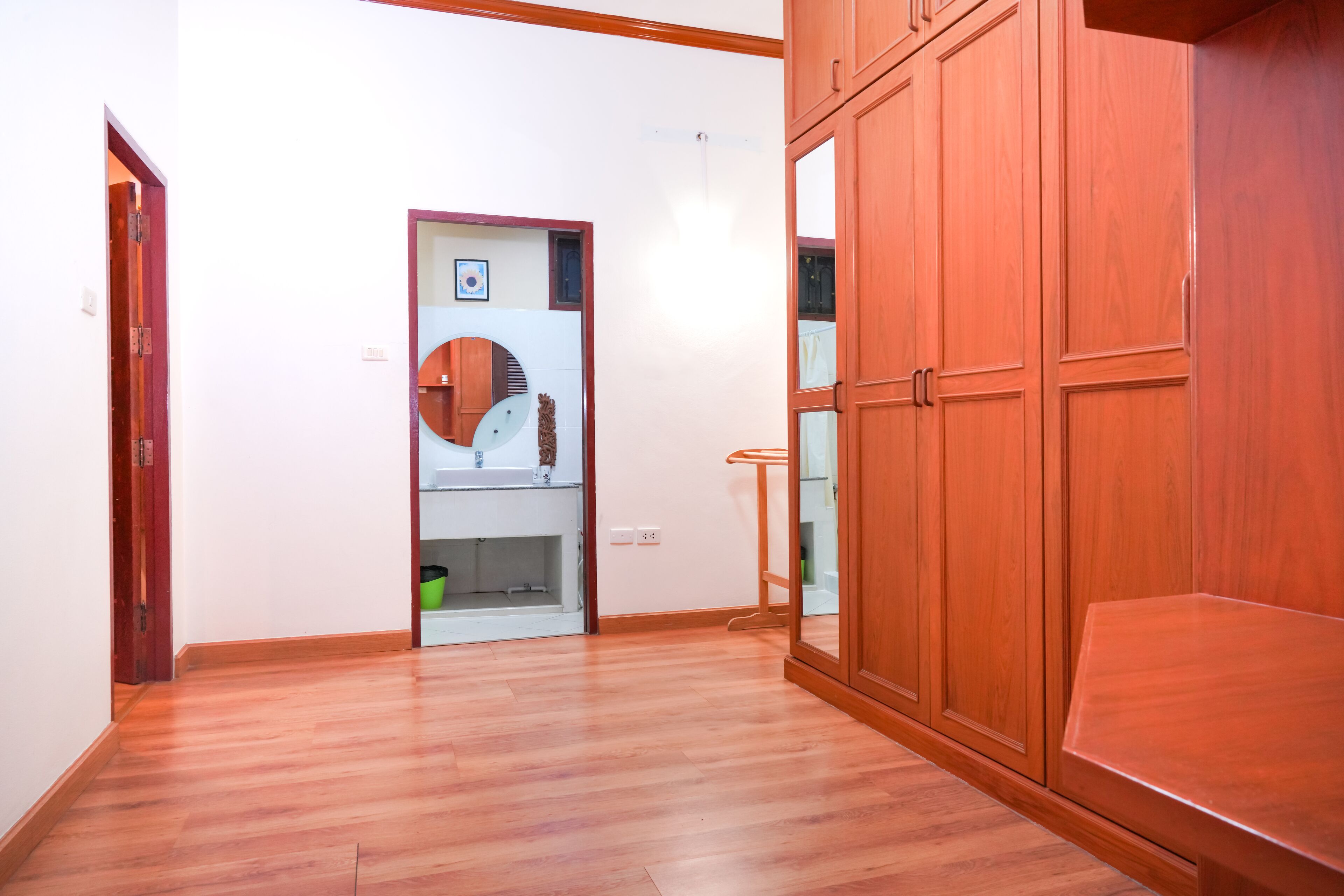 Una habitación con suelo de madera, un armario de madera y un espejo.