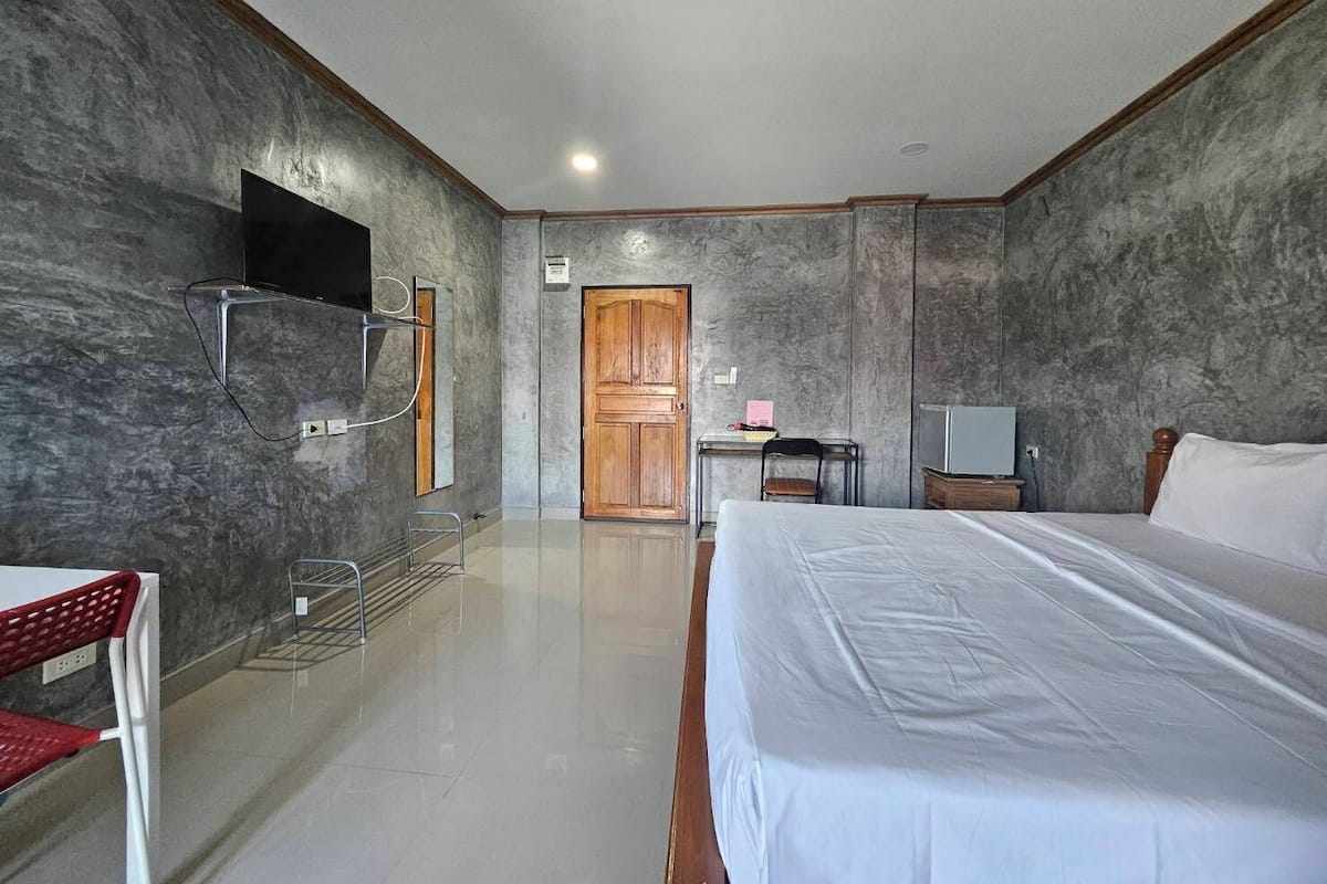Habitación de hotel con una cama grande, televisión, escritorio y silla, y una puerta de madera.