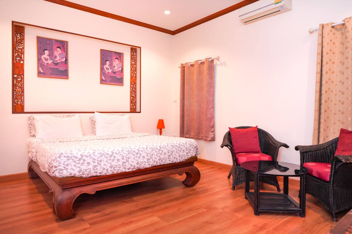Un dormitorio con una cama de madera, dos sillas con cojines rojos y dos cuadros en la pared.