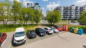 A parking area with several cars, a red trash bin, and a gas station. - Family Apartment with Parking | Balcony and Workspace (Warszawa)