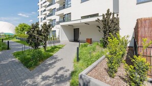 A modern building with a flat roof, multiple balconies, and a paved walkway with greenery. - Family Apartment with Parking | Balcony and Workspace (Warszawa)
