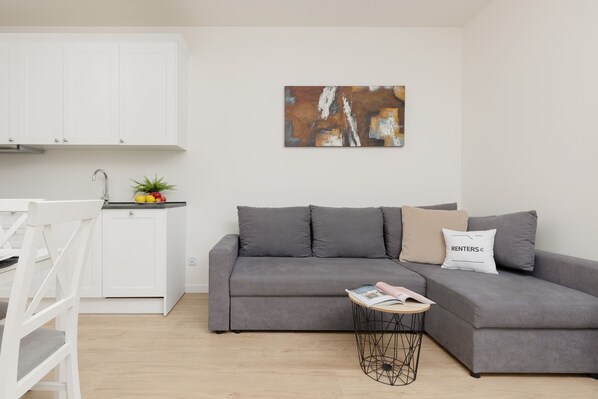 Ein modernes Wohnzimmer mit einem grauen Sofa, einem kleinen runden Couchtisch und einem weißen Schrank.