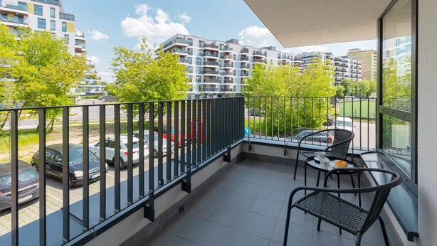 A balcony with a view of a parking lot and surrounding buildings. - Family Apartment with Parking | Balcony and Workspace (Warszawa)