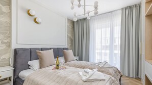 A modern hotel room with a large bed, a bedside table, a nightstand, a chandelier, and a view of the city through large windows. - Elegant Apartment on Salt Island | Parking | Balcony (Kolobrzeg)