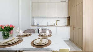 A modern kitchen with white cabinets, a marble countertop, and a dining area set with plates, cutlery, and wine glasses. - Elegant Apartment on Salt Island | Parking | Balcony (Kolobrzeg)