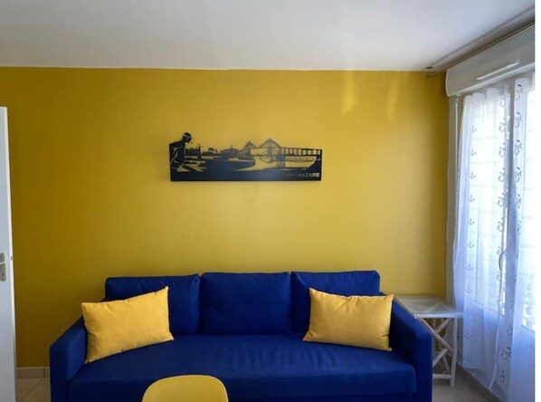 Relax in this inviting living room with a blue sofa, yellow cushions, and a coastal-themed artwork.