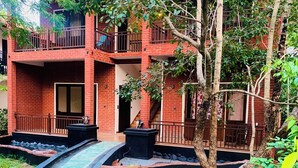 Un edificio a più piani con facciata in mattoni, una piccola area giardino con vialetto lastricato e un albero in primo piano.