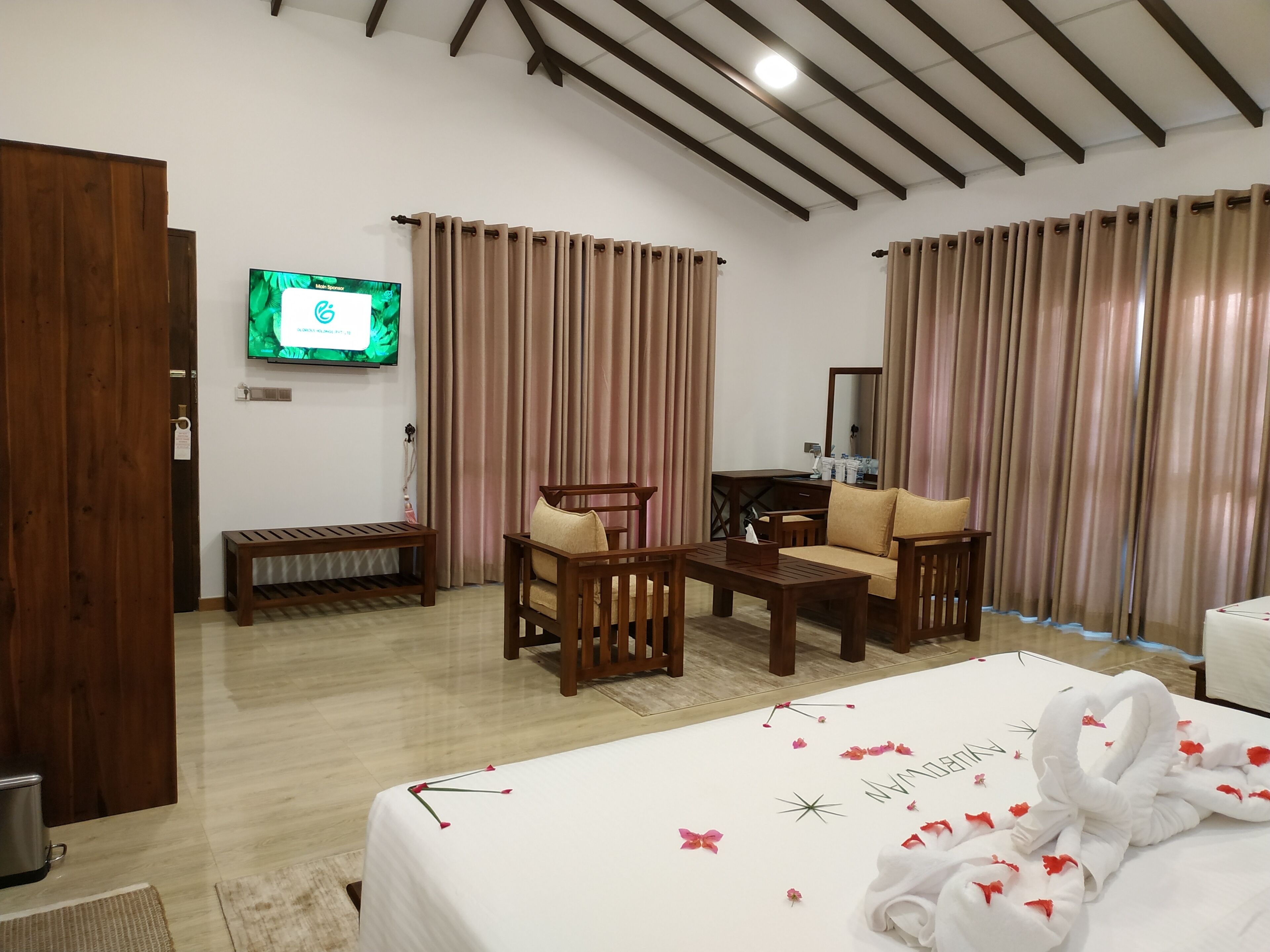 A hotel room with a bed, a wooden bench, a sofa, a small table, a TV, and curtains.