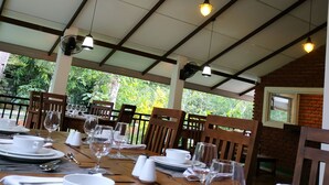 Zona pranzo con tavoli apparecchiati per due, completa di stoviglie e bicchieri bianchi, sotto un soffitto con travi a vista e lampade a sospensione.