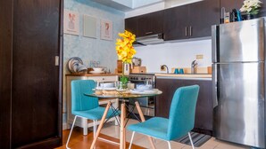 Cocina moderna con gabinetes de madera oscura, refrigerador de acero inoxidable y un comedor con sillas color turquesa y una mesa de vidrio.