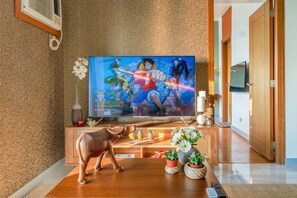 A living room with a television displaying an anime, a wooden cabinet with decorative items, and a plush toy on the floor. - Eton Bay  (Manila)