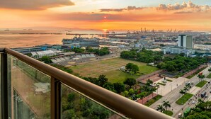 Un paisaje urbano con un atardecer sobre el agua, que muestra edificios industriales, una amplia plaza abierta y un edificio blanco destacado.