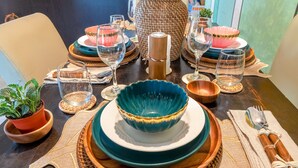 Una mesa dispuesta con varios platos, tazones y vasos, con una planta en maceta y una vela.